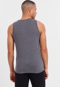 Gray cotton tank top with a round neckline, sleeveless design, and a smooth texture, shown from the back, paired with black pants.