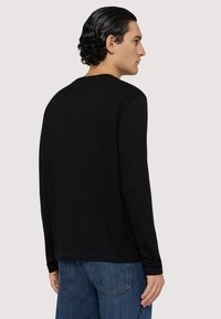 Czarny long-sleeve t-shirt z okrągłym dekoltem, wykonany z miękkiego materiału, przedstawiony z tyłu, w połączeniu z niebieskimi dżinsami.