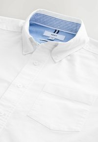 Chemise blanche boutonnée, en coton, avec col, dotée d'un col intérieur à fines rayures bleu clair et d'une poche poitrine.