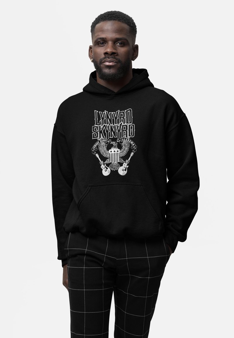 Sudadera negra con un gráfico blanco que presenta un águila y guitarras. Fabricada con un tejido de textura suave. Con un bolsillo frontal tipo canguro. Pantalones de cuadros negros.