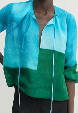 Personne portant un chemisier ample à manches longues avec un dégradé bleu-vert et un profond col en V avec des liens fins suspendus.