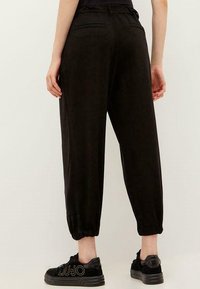 Zwarte, taps toelopende joggingsbroek met elastische boorden en twee achterzakken, gemaakt van een zachte stof. Gecombineerd met zwarte sneakers met logodetails.