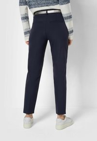 Pantaloni tailored blu con vestibilità slim, dotati di tasche laterali, tasche posteriori a filetto e una finitura in tessuto liscia. Abbinati a sneakers bianche.