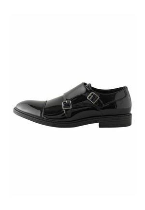 Schwarzer lacklederner Schuh mit zwei seitlichen Schnallen, abgerundeter Zehenpartie und niedrigem Absatz. Glatte Textur mit sichtbarem Steppdetail.