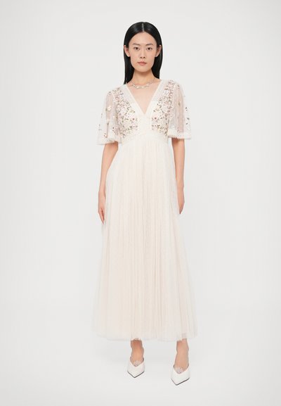 Μακρύ ελεφαντόδοντο φόρεμα με λουλουδάτη κεντητική στο μπούστο, διάφανα μανίκια που φτερουγίζουν και υφή με πιέτες στην φούστα. Φοριέται με λευκές γόβες.