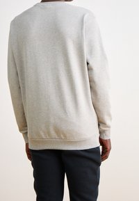 Sudadera gris con mangas largas, cuello redondo y puños de canalé; textura suave con un ajuste ligeramente relajado. Diseño liso, sin patrones.