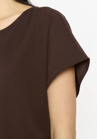 Top corto marrone con maniche a sbuffo, realizzato in tessuto morbido con una texture liscia, caratterizzato da un collo rotondo e dettagli cuciti sottili lungo le cuciture.