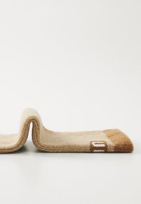 Ullsocka med en beige kropp och en brun tå; har en vit etikett sydd på sidan. Mjuk textur och i en vikad position.
