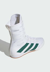 Scarpa sportiva bianca con design alto, caratterizzata da un materiale testurizzato, dettagli verde con tre strisce e una suola di gomma.