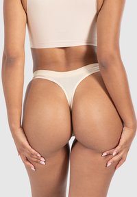 Beige nahtloser Tanga mit breitem elastischem Bund, der eine glatte Textur und ein minimalistisches Design mit minimaler Bedeckung bietet und die Hinteransicht betont.