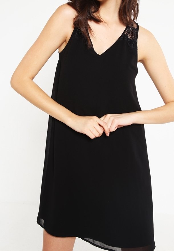 Svart ärmlös klänning med V-halsringning och spetsdetaljer på ena axeln. Tillverkad av lätt, flödande tyg med en mjuk textur.