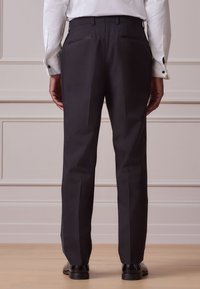 Pantaloni neri su misura con silhouette dritta, caratterizzati da due tasche posteriori e una texture del tessuto liscia. Indossati con una camicia bianca.