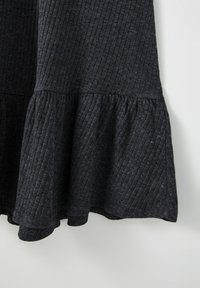 Tissu côtelé gris foncé avec un ourlet à volant évasé, montrant la texture et des lignes verticales sur la partie inférieure d'un vêtement.