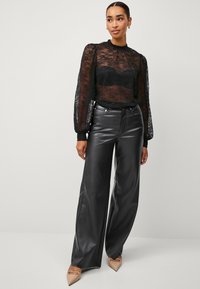 Zwarte kanten top met lange mouwen en transparante panelen, gecombineerd met hoogoplopende zwarte nepleer wijde broek en nude puntige hakken.