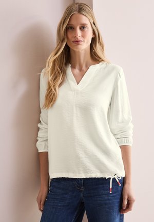 Lichtgroene, gestructureerde blouse met een V-hals en lange mouwen. Heeft elastieken manchetten en een trekkoord onderkant met rode accenten. Casual pasvorm.