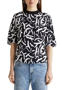 Haut à manches courtes noir et blanc à motif, avec un col rond et une coupe décontractée, fabriqué en tissu léger, porté avec un jean bleu.