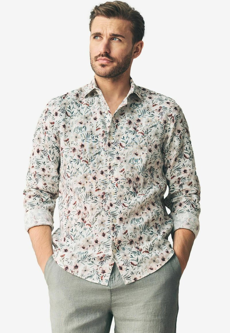 Chemise à manches longues à motif floral avec un fond blanc, ornée de fleurs multicolores et de feuilles vertes. Col à boutons, coupe classique.