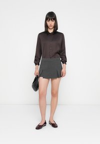 Chemise noire en satin à boutons avec des manches longues, associée à une mini-jupe plissée grise, un sac à main noir et des ballerines bordeaux.