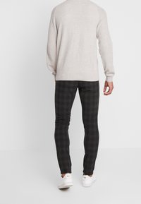 Ljusgrå stickad tröja och svarta rutiga byxor, med en avkopplad passform och texturerad tyg. Vita sneakers fulländar outfiten.