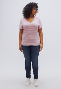 Ροζ ριγέ t-shirt με V λαιμόκοψη, κοντά μανίκια, συνδυασμένο με σκούρο μπλε στενά τζιν και λευκά αθλητικά παπούτσια. Απλός σχεδιασμός και casual εφαρμογή.