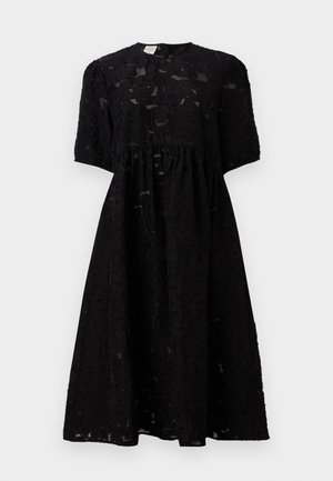 Fekete ruha textúrált anyagból, rövid ujjakkal, kerek nyakkivágással és ráncolt derékvonallal, amely éppen térd alatt ér véget.