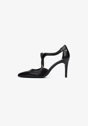 Zapato de tacón alto de cuero negro con punta afilada, diseño de tira en forma de T, acentos recortados y un tacón delgado. Detalle de hardware dorado incluido.