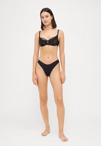 Zwart lingerie set met een sheer kanten beha met onderbeugels en bijpassende low-rise slipjes. Glad textuur, minimalistisch ontwerp en geen versieringen.