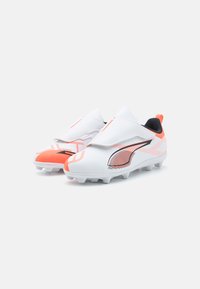 Bottes de football blanches avec des accents orange et un intérieur noir, présentant un dessus synthétique lisse, un design sans lacets et une semelle à crampons.