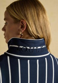 Tumestriipidega särk, millel on valged triibud ja mille krae on kaunistatud tikitud "JOULES" logoga. Sile tekstuur, nähtavad õmbluse detailid.