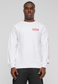 White long-sleeve t-shirt featuring red text and logo on the chest and sleeve, made from soft cotton material, with a relaxed fit.