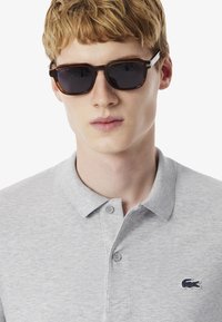 Sunglasses med mörka linser och sköldpaddsmönstrad ram, ihop med en ljusgrå polo-skjorta med en liten logotyp och knappad krage.