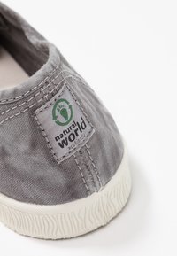 Scarpa slip-on in tela grigia con suola in gomma bianca, caratterizzata da un design cucito e un'etichetta verde con il logo "natural World".