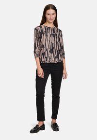 Schwarzes und pinkes gemustertes Langarmshirt, kombiniert mit schwarzen Slim-Fit-Hosen und schwarzen Loafers, mit einem runden Halsausschnitt und hochgeklappten Ärmeln.