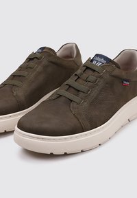 Zapatillas de cuero verde oliva con suelas de goma beige, con punta redondeada, cierre de cordones y detalles de costura en contraste.