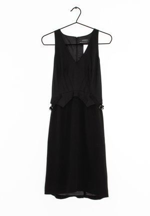 Zwarte jurk met een V-hals en mouwloos ontwerp. Heeft een aansluitend lijfje, een lichte peplum bij de taille en de stoftextuur is glad.