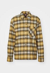 Camicia a quadri di flanella gialla, nera e bianca. Presenta una tasca frontale, chiusura con bottoni, maniche lunghe e collo classico.