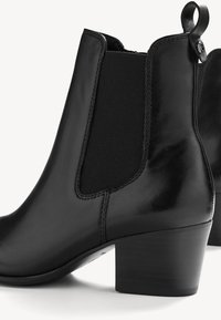 Bottines en cuir noir avec panneaux latéraux élastiques, une boucle à l'arrière et des talons blocs bas sur fond blanc.