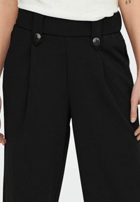 Sorte bukser med skræddersyet design, høj talje og to knapper foran. Glat, struktureret stof med plisseringer for ekstra detaljer.