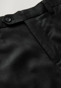 Pantalons noirs ajustés avec une texture lisse, dotés d'une fermeture à bouton et de coutures soignées le long de la taille et de la zone du zip.