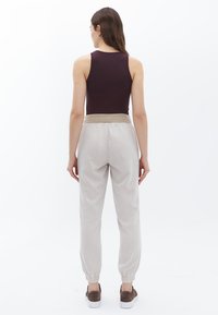 Bruine tanktop en lichtbeige joggers met elastieken boorden. De joggers hebben een zachte textuur en een verstelbare tailleband.