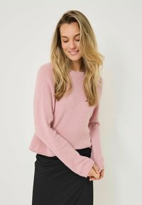 Hellrosa, flauschiger Pullover mit Rundhalsausschnitt und langen Ärmeln, kombiniert mit einem schwarzen Rock. Weicher Stoff und entspannte Passform.