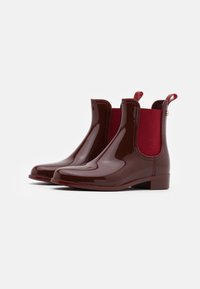 Botines burdeos de tobillo con parte superior de goma brillante, paneles laterales elásticos y tacón bajo. Tiradores reforzados para facilitar el calzado. Textura suave.