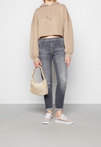Sudadera corta beige, pantalones ajustados gris y zapatillas beige claras. Accesorio: pequeño bolso de crema. Tejido suave y diseño casual.