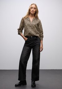 Beige bluse med leopardmønster, v-udskæring og samlede ærmer, parret med højtaljede sorte bredbenspants og sorte ankelstøvler.