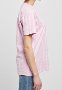 Růžové pruhované tričko s krátkým rukávem, vyrobené z bavlny. Má vertikální bílé pruhy, volný střih a kulatý výstřih.