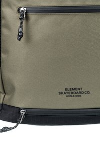 Olive green backpack with a textured surface, featuring a black zipper and logo “ELEMENT SKATEBOARD CO” at the bottom. Two zippered pockets available.