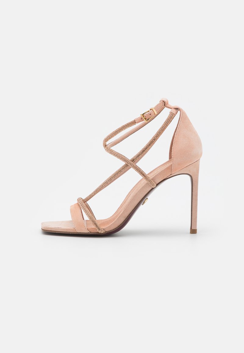 Beige suede high-heeled sandal featuring crisscross straps with metallic detailing, an open toe, and a slender stiletto heel.