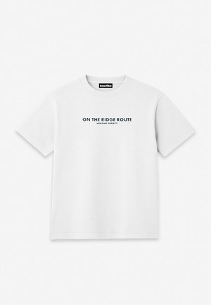 Bijela majica kratkih rukava s okruglim izrezom, s crnim tekstom "ON THE RIDGE ROUTE KAOTIKO SOCIETY" smještenim u sredini prsa.