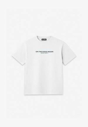 Camiseta blanca de manga corta con cuello redondo y texto negro "ON THE RIDGE ROUTE KAOTIKO SOCIETY" centrado en el pecho.