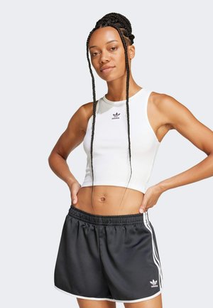 White fitted crop top with ribbed texture and black adidas logo, paired with black athletic shorts featuring white side stripes and elastic waistband.